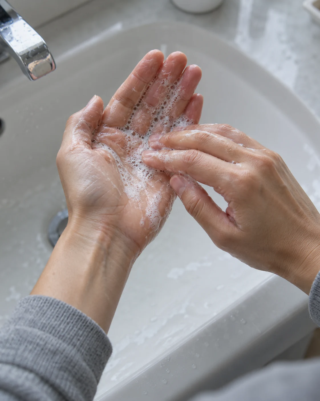 Close cleansing detail of hands working a small amount of fine lather above a grey basin